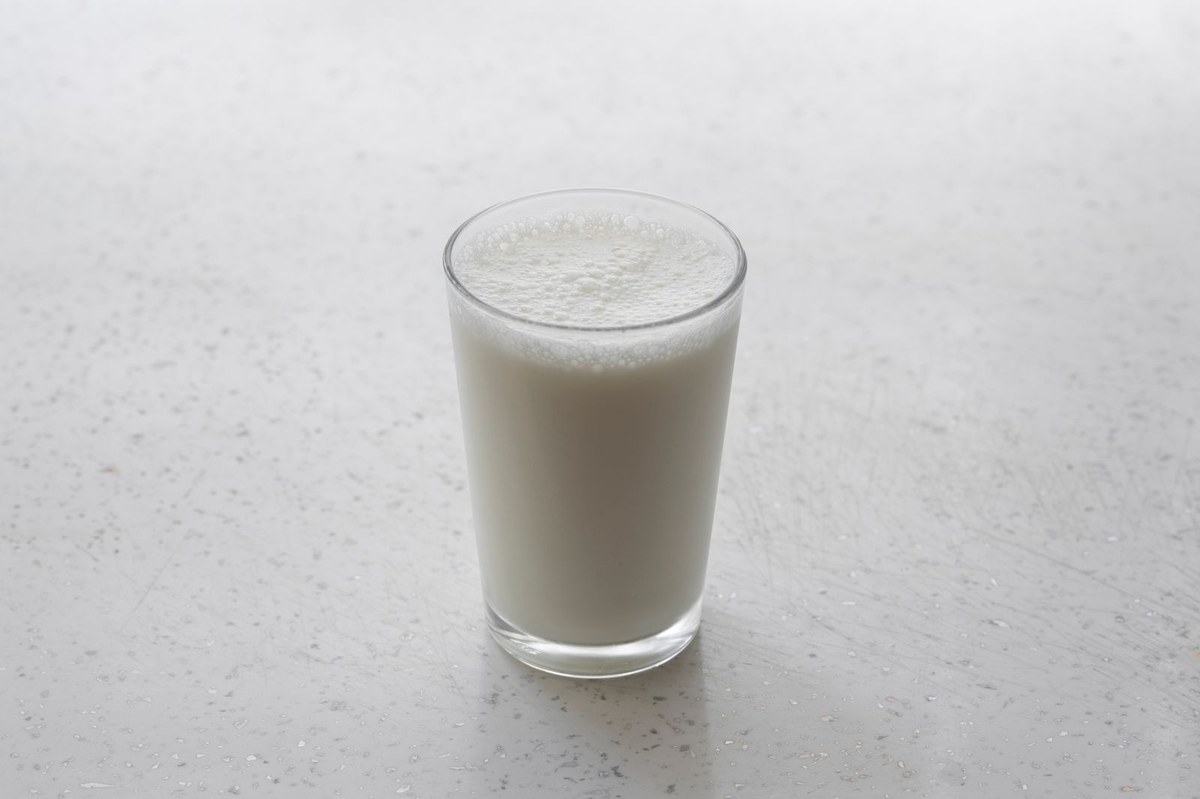 Clear glass of frothy white milk standing alone on a pale speckled countertop