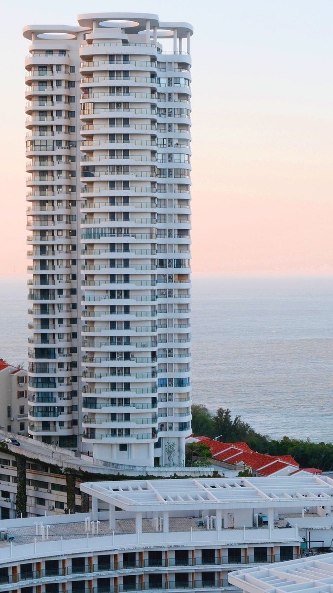 Tall white residential tower with rounded balconies beside the sea at sunset